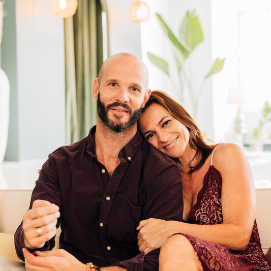 Man and woman sitting close together on a couch in a bright room with plants.