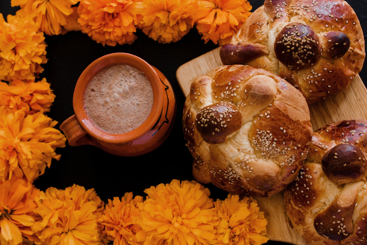 Bread, a cup of cacao, and marigold flowers on a dark background