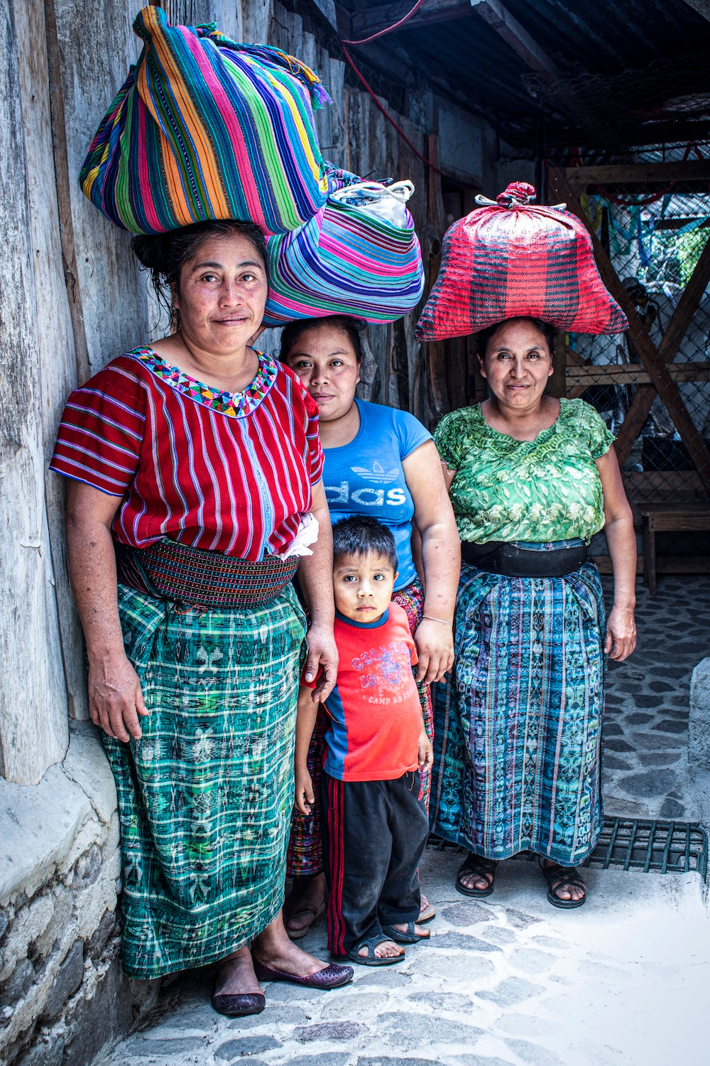 Keith's Cacao tostadoras and one of their children standing together, wearing traditional clothing and carrying cacao beans on their heads that they will take home to lightly toast and hand-peel..